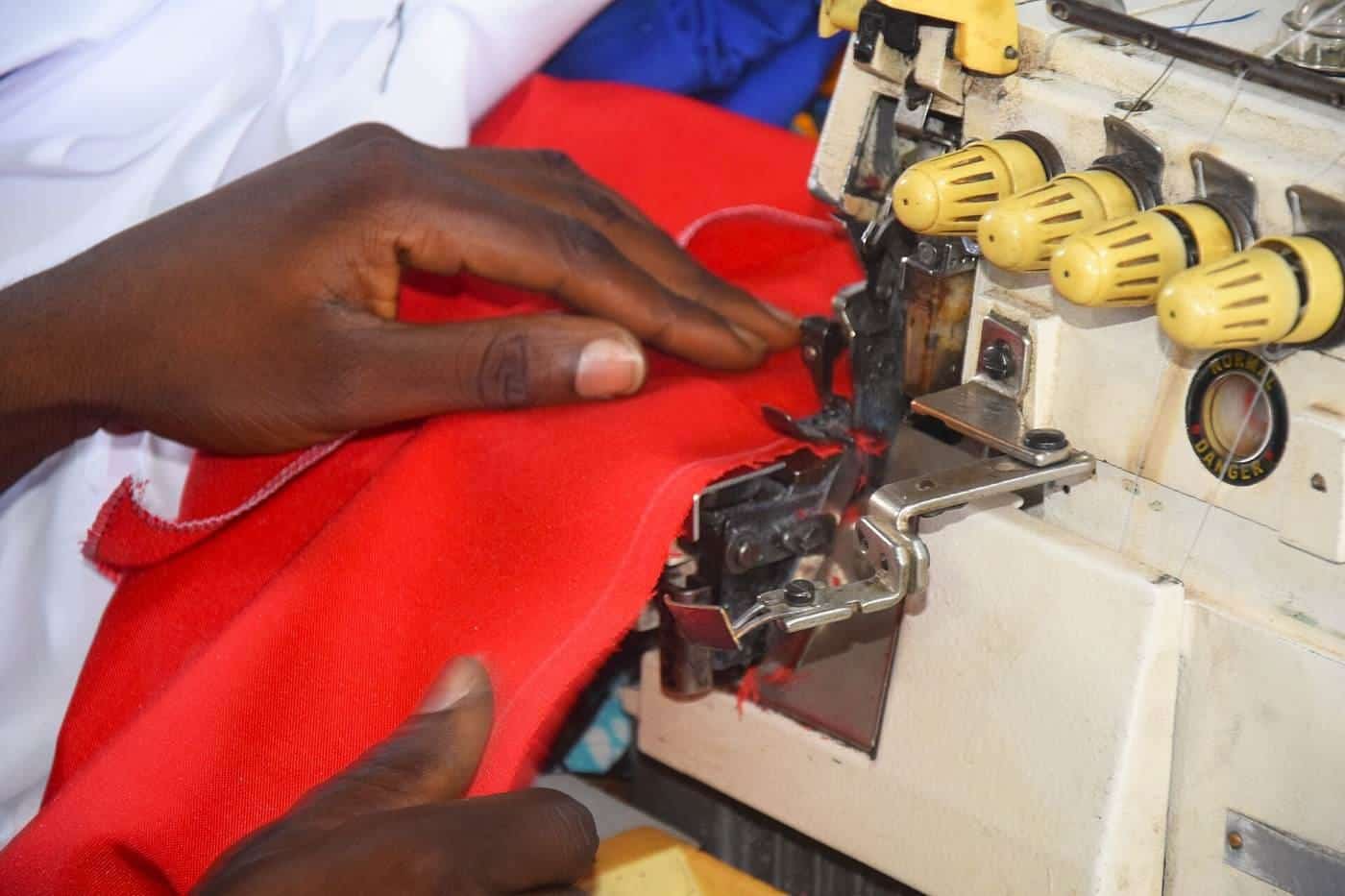 Hands guiding red fabric through an overlocker sewing machine