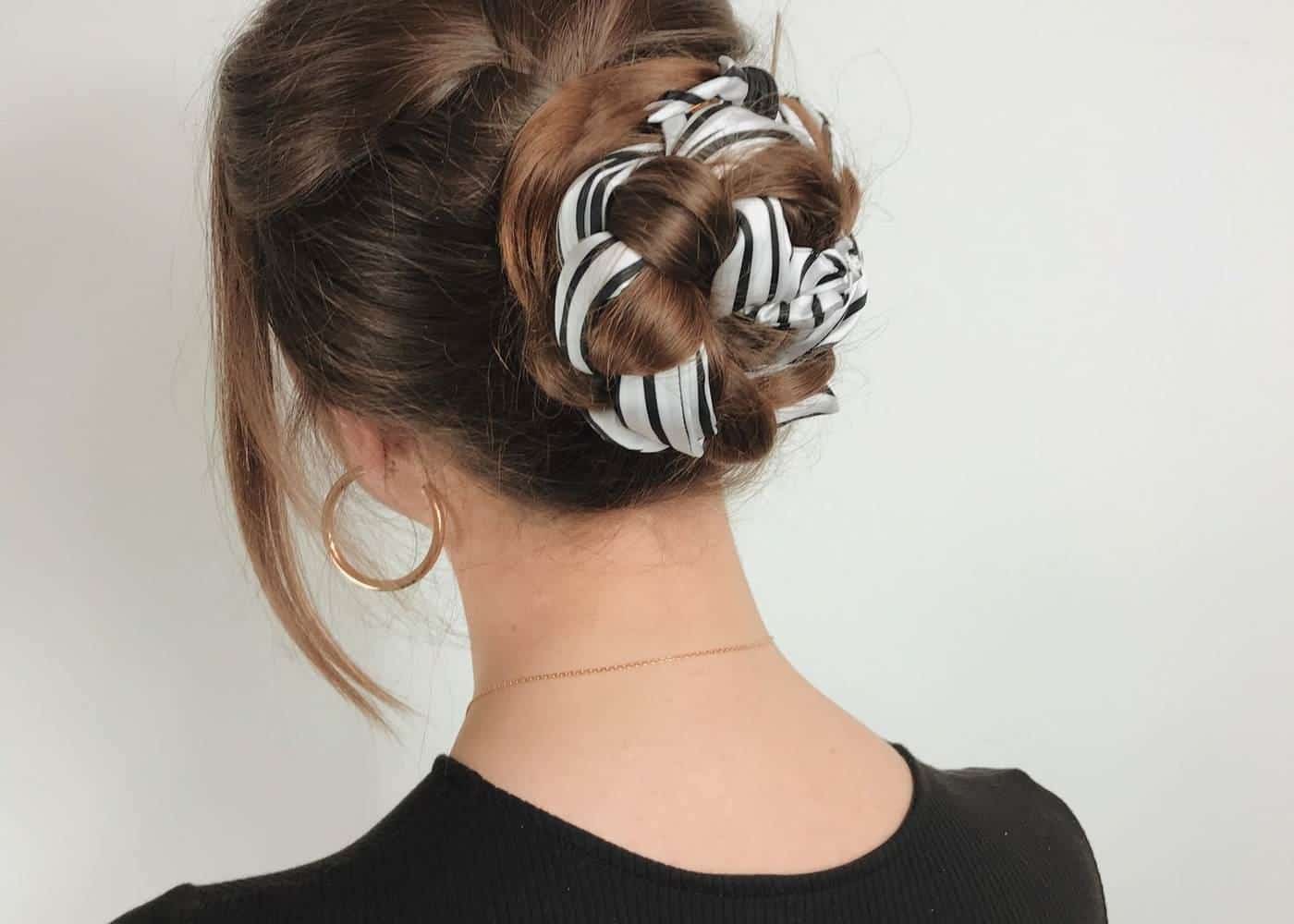 A woman with a patterned scrunchie holding her hair in a loose bun